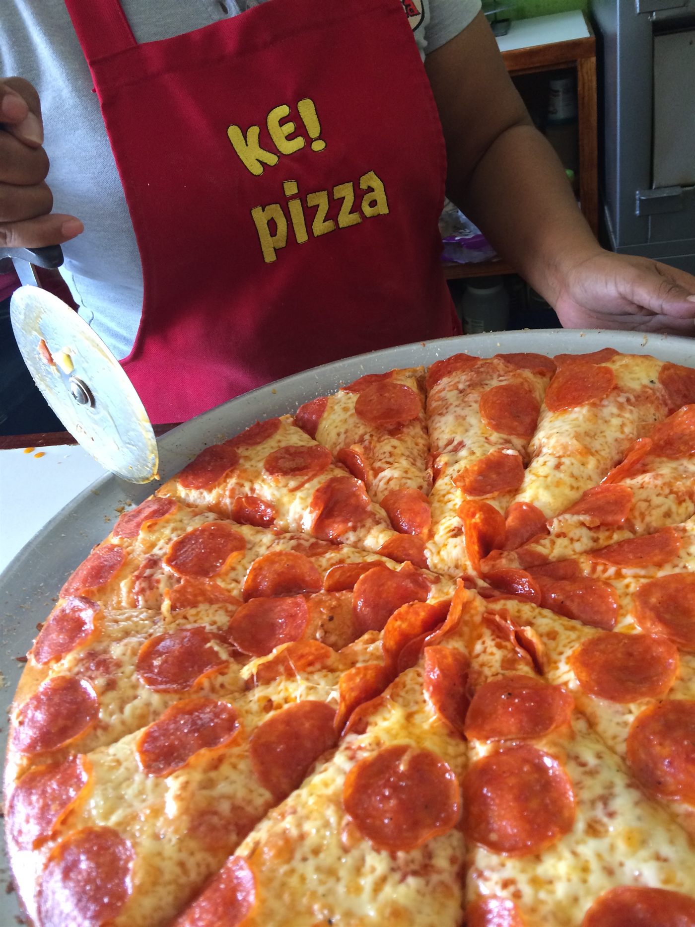 Pizza de pepperoni recién horneada en Ke Pizza, servida por una empleada con el mandil de la casa